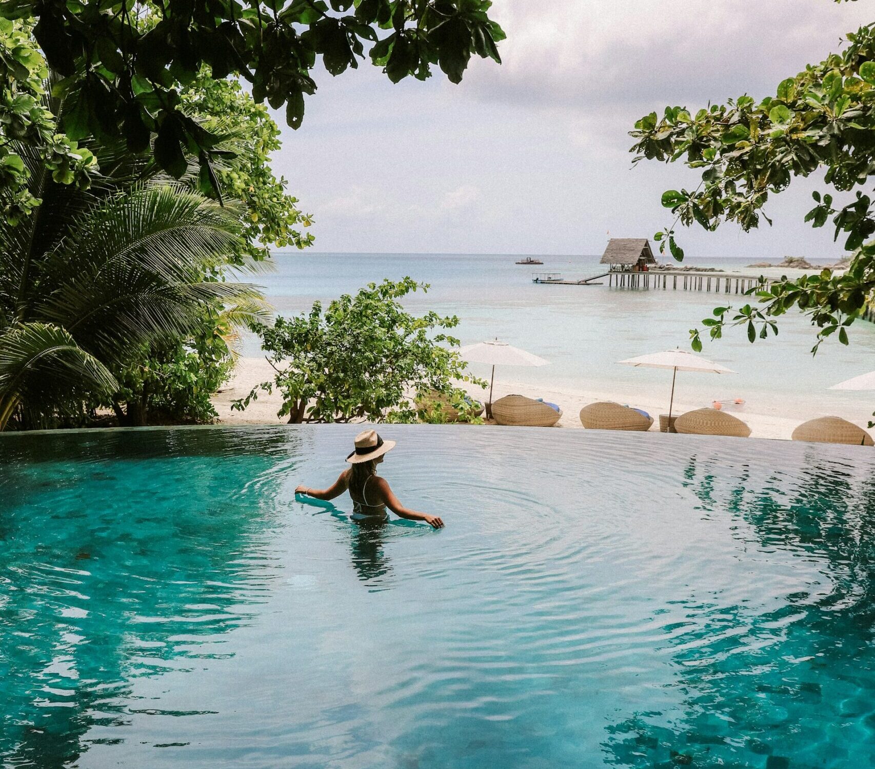 infinity pool looking out over tripical beach and ocean with woman lounging in middle of pool