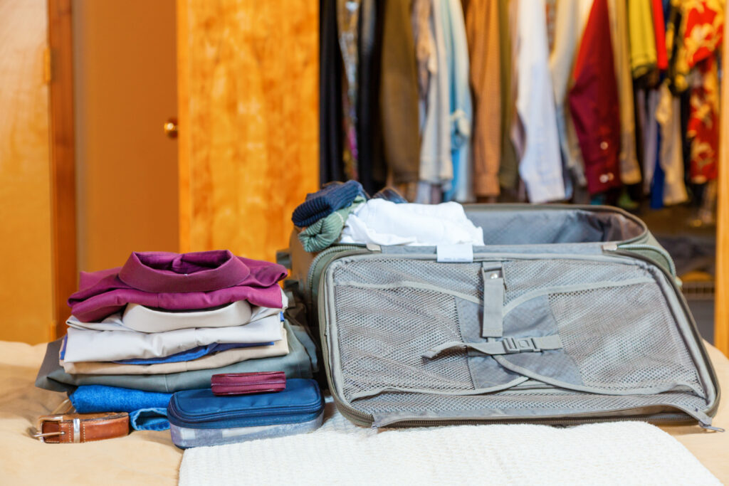 open suitcase with folded clothing inside and next to it. behind the suitcase is a closet full of hanging clothes