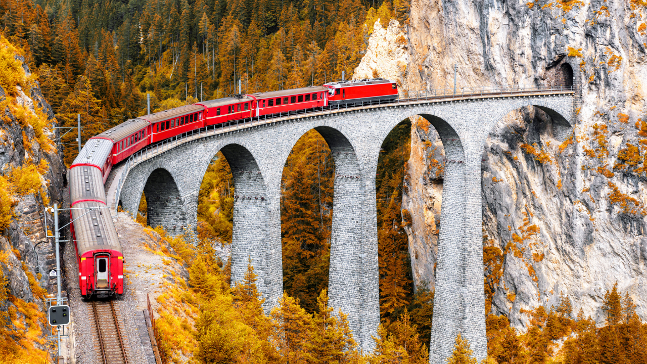 red train traversing across a stone brigde and into tunnel