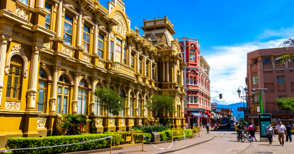 A street scene with ornate yellow and red buildings under a bright blue sky.